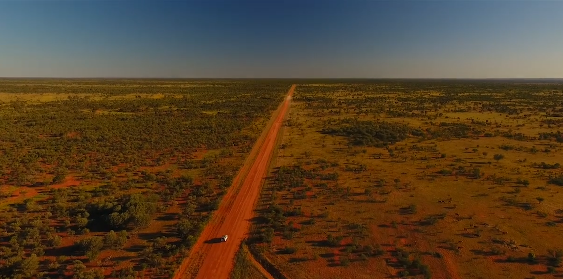 Aerial view of a red dirt road running straight across the outback at dusk