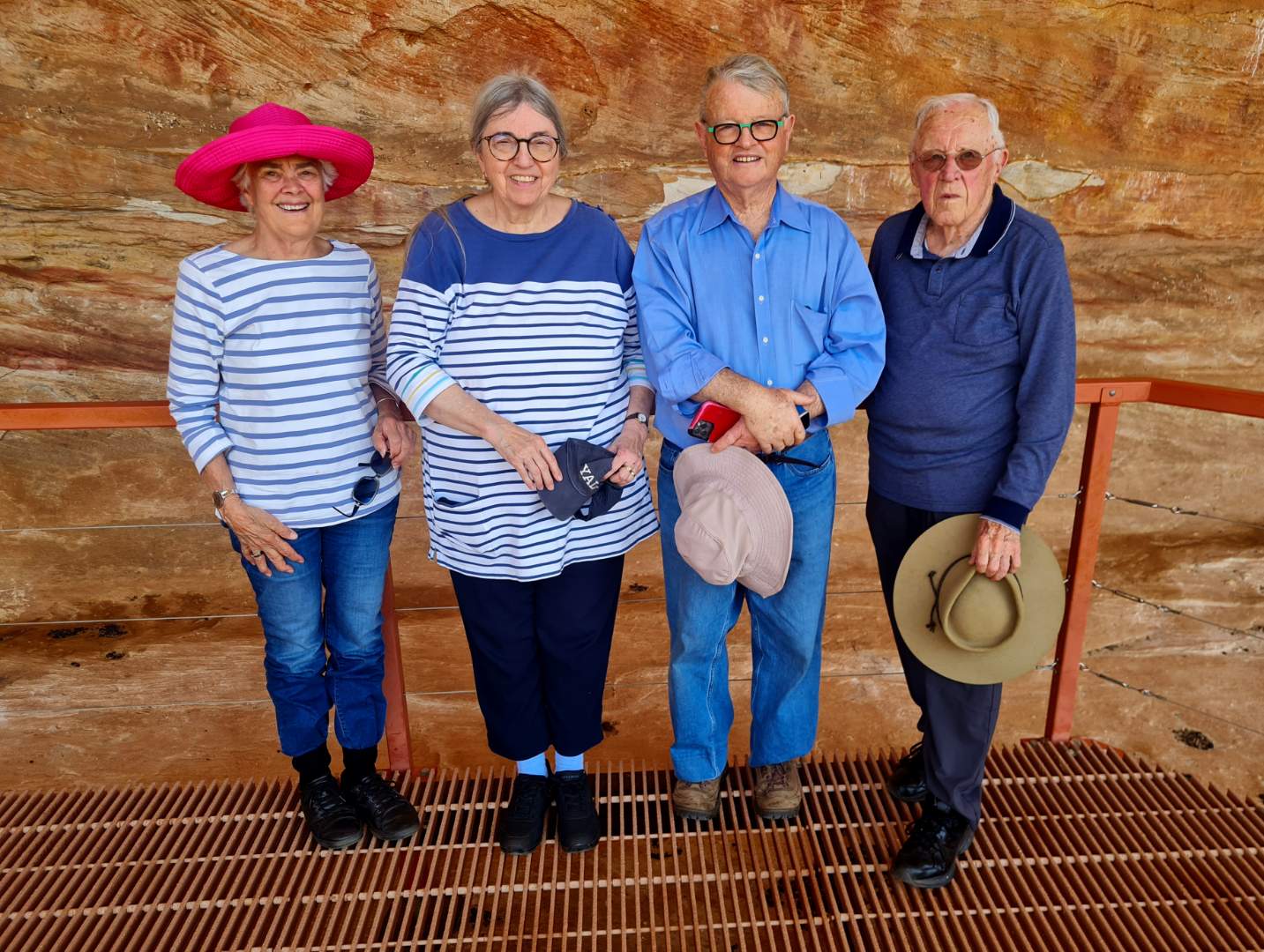 Four guests in hats on a viewing platform in front of a red rock wall