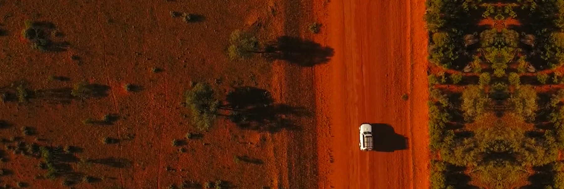 Aerial view of a vehicle on a red outback road between saltbush
