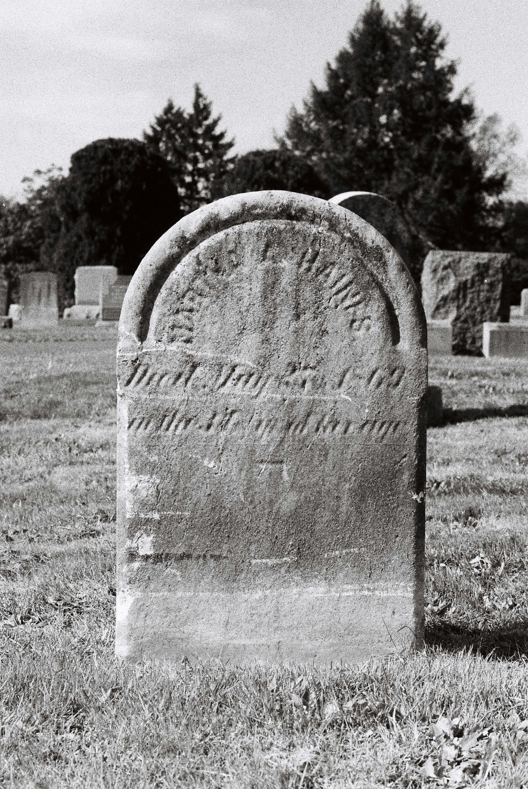 Weathered old headstone in a grassy pioneer graveyard